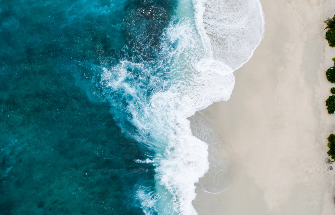Aerial view of teal ocean waves breaking into white foam off the coast of Oʻahu